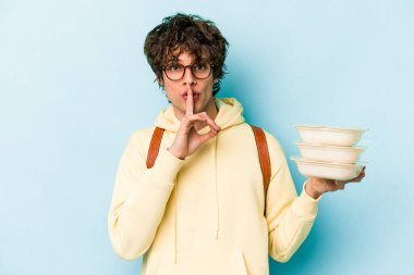 Beyaz tenli genç bir öğrenci mavi arka planda saklanmış bir saklama kabı tutuyor ya da sessizlik istiyor..