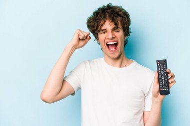 Elinde televizyon kumandası olan beyaz bir adam mavi arka planda izole edilmiş zafer ve galibiyet kavramından sonra yumruk kaldırıyor..