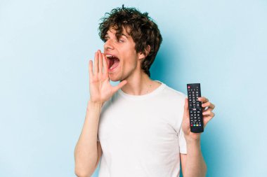 Elinde televizyon kumandası olan beyaz bir adam mavi arka planda izole edilmiş bağırıyor ve avuç içini açık tutuyor..