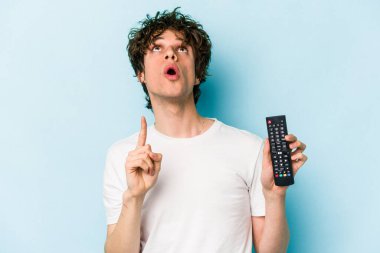 Elinde televizyon kumandası olan beyaz bir adam mavi arka planda izole edilmiş ve ağzı açık bir şekilde üst tarafı işaret ediyor..