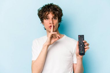 Elinde televizyon kumandası olan beyaz bir adam mavi arka planda izole edilmiş bir şekilde bir sır saklıyor veya sessizlik istiyor..