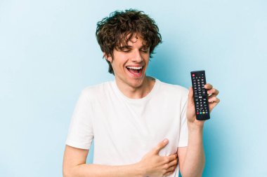 Elinde televizyon kumandası olan beyaz bir adam mavi arka planda izole edilmiş gülüyor ve eğleniyor..