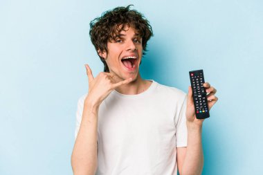 Elinde televizyon kumandası olan beyaz bir adam mavi arka planda izole edilmiş. Cep telefonu hareketini parmaklarıyla gösteriyor..