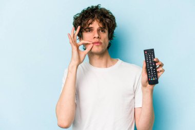 Elinde televizyon kumandası olan beyaz bir adam mavi arka planda izole edilmiş ve parmakları dudaklarında bir sır saklıyor..