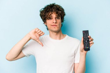 Elinde televizyon kumandası olan beyaz bir adam mavi arka planda izole edilmiş. Sevimsiz bir hareket gösteriyor. Anlaşmazlık konsepti.