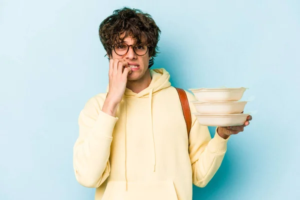 Joven Estudiante Caucásico Sosteniendo Tupperware Aislado Sobre Fondo Azul Mordiendo — Foto de Stock