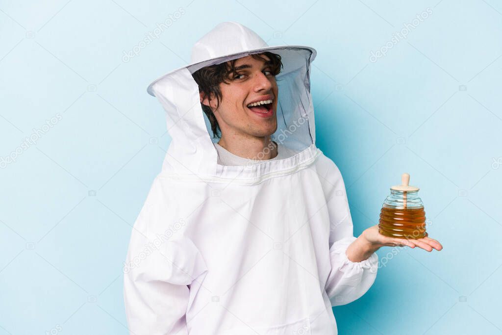 Young caucasian beekeeper man isolated on blue background looks aside smiling, cheerful and pleasant.