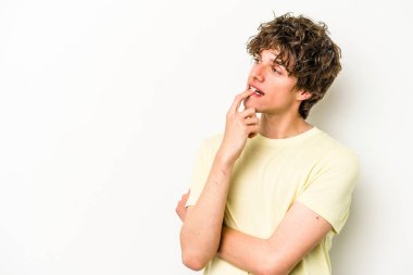 Beyaz arka planda izole edilmiş genç beyaz bir adam şüpheli ve şüpheci bir ifadeyle yana bakıyor..