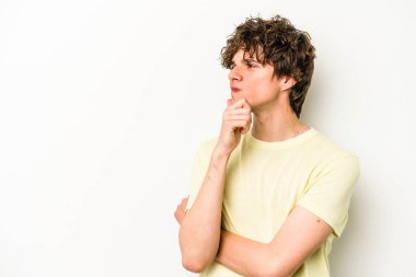 Beyaz arka planda izole edilmiş genç beyaz bir adam şüpheli ve şüpheci bir ifadeyle yana bakıyor..