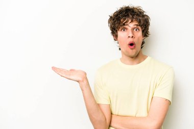 Beyaz arka planda izole edilmiş genç beyaz adam, avuç içi fotokopi alanını elinde tutmaktan etkilenmiş..