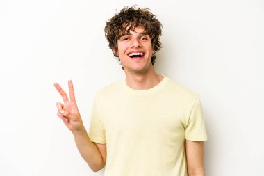 Beyaz arka planda izole edilmiş genç beyaz bir adam zafer işareti gösteriyor ve gülümsüyor..