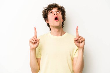 Beyaz arka planda izole edilmiş genç beyaz adam ağzı açık bir şekilde üst tarafı işaret ediyor..