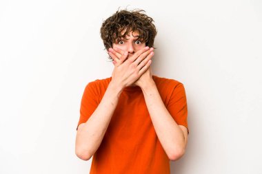 Beyaz arka planda izole edilmiş genç beyaz adam elleriyle ağzını kapatırken şok oldu..