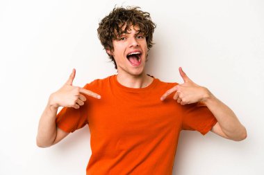 Beyaz arka planda izole edilmiş genç beyaz bir adam parmağını göstererek şaşırdı, geniş bir gülümsemeyle..