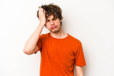 Beyaz arka planda izole edilmiş genç beyaz bir adam yorgun ve uykulu bir şekilde elini başının üstünde tutuyor..