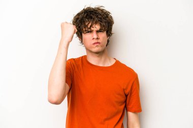 Beyaz arka planda izole edilmiş genç beyaz bir adam yumruğunu kameraya gösteriyor, agresif bir yüz ifadesi..