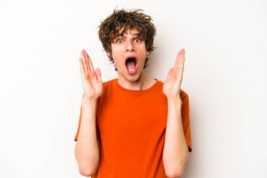 Beyaz arka planda izole olmuş genç beyaz bir adam zaferi veya başarıyı kutluyor, şaşırıyor ve şok oluyor..
