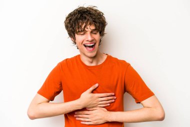 Beyaz arka planda izole genç beyaz adam mutlu bir şekilde gülüyor ve ellerini karnının üstünde tutarak eğleniyor..