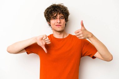 Beyaz arka planda izole edilmiş genç beyaz bir adam baş parmaklarını aşağı ve yukarı kaldırıyor, zor seçim konsepti