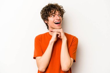 Beyaz arka planda izole genç beyaz adam ellerini çenesinin altında tutuyor, mutlu bir şekilde yana bakıyor..