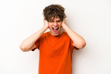 Beyaz arka planda izole edilmiş genç beyaz bir adam kulakları kulaklarıyla kapatıyor ve çok ses duymamaya çalışıyor..
