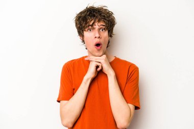 Beyaz arka planda izole edilmiş genç beyaz bir adam şans için dua ediyor, şaşırmış ve ağzını açıp önüne bakıyor..