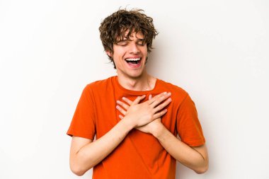 Beyaz arka planda soyutlanmış beyaz tenli genç bir adam gülüyor, elini yüreğine koyuyor, mutluluk kavramını koruyor..