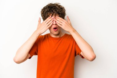 Beyaz arka planda izole edilmiş genç beyaz bir adam elleriyle gözlerini kapatmaktan korkuyor..