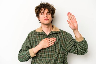 Beyaz arka planda izole edilmiş genç beyaz adam yemin ediyor, elini göğsüne koyuyor..