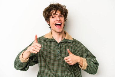 Beyaz arka planda izole edilmiş genç beyaz bir adam iki parmağını da kaldırıyor, gülümsüyor ve kendinden emin..