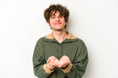 Beyaz arka planda izole edilmiş genç beyaz bir adam elinde avuç içi bir şeyle kameraya sunuyor..