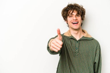 Beyaz arka planda izole edilmiş genç beyaz adam gülümsüyor ve başparmağını kaldırıyor.