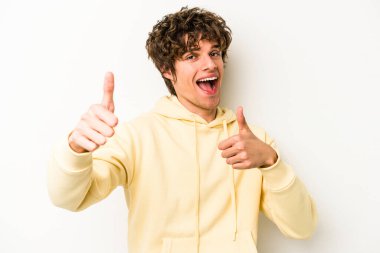 Beyaz arka planda izole edilmiş genç beyaz bir adam iki parmağını da kaldırıyor, gülümsüyor ve kendinden emin..