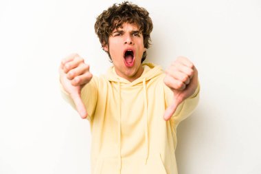 Beyaz arka planda izole edilmiş genç beyaz bir adam baş parmağını aşağı gösteriyor ve hoşlanmadığını ifade ediyor..