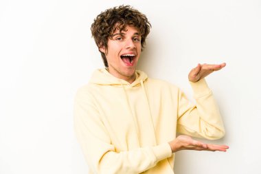 Beyaz arka planda izole edilmiş genç beyaz bir adam işaret parmaklarıyla küçük bir şey tutuyor, gülümsüyor ve kendinden emin..