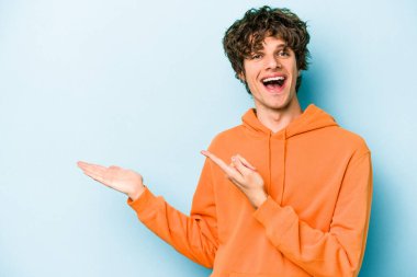 Kafkasyalı genç adam mavi arka planda izole edilmiş. Elinde palmiye ağacının bir kopyası olduğu için heyecanlı..