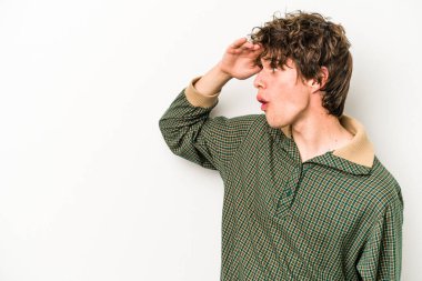 Beyaz arka planda izole edilmiş genç beyaz bir adam uzaklara bakıyor ve elini alnına koyuyor..