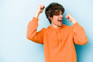 Mavi arka planda izole edilmiş genç beyaz bir adam zaferden sonra yumruğunu kaldırıyor, kazanan konsept..