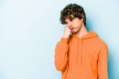 Mavi arka planda izole edilmiş, üzgün ve dalgın hisseden, kopyalama alanına bakan genç beyaz bir adam..