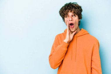 Mavi arka planda izole edilmiş genç beyaz bir adam gizli bir sıcak fren haberi veriyor ve yana bakıyor.