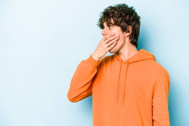 Kafkasyalı genç adam mavi arka planda izole edilmiş. Düşünceli bir şekilde ağzıyla ağzını kapatan bir fotokopi odasına bakıyor..