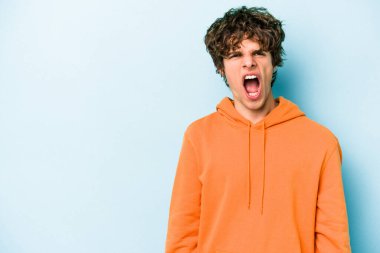 Kafkasyalı genç adam mavi arka planda izole edilmiş. Çok kızgın, öfkeli, hayal kırıklığına uğramış..