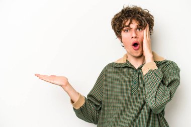 Beyaz arka planda izole edilmiş genç beyaz adam, avuç içi fotokopi alanını elinde tutmaktan etkilenmiş..