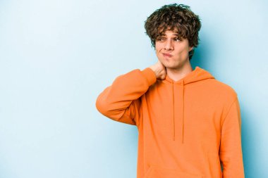 Kafkasyalı genç adam mavi arka planda izole edilmiş kafasının arkasına dokunuyor, düşünüyor ve bir seçim yapıyor..