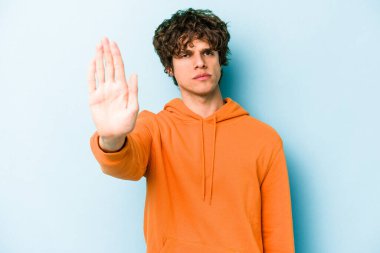 Mavi arka planda izole edilmiş genç beyaz adam elini uzatmış, dur işareti göstererek seni engelliyor..
