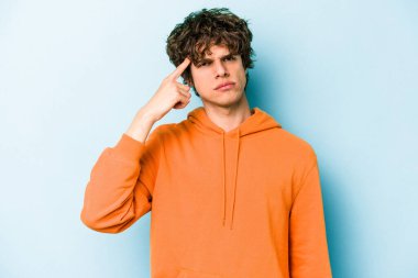 Mavi arka planda izole edilmiş genç beyaz bir adam şakağı parmağıyla işaret ediyor, düşünüyor ve bir göreve odaklanıyor..