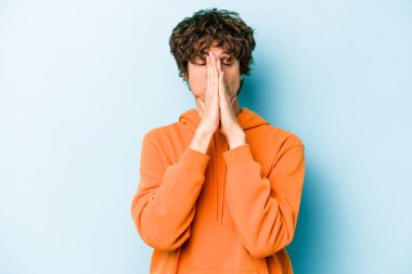 Mavi arka planda izole edilmiş genç beyaz bir adam el ele tutuşup, ağzının kenarında dua ediyor, kendinden emin..