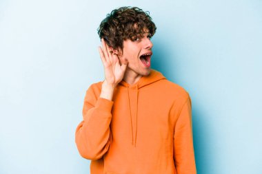 Mavi arka planda izole edilmiş genç beyaz adam bir dedikoduyu dinlemeye çalışıyor..