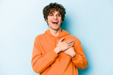 Mavi arka planda izole edilmiş beyaz bir genç, dost bir ifadeye sahip, avuçlarını göğsüne bastırıyor. Aşk konsepti.