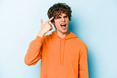 Mavi arka planda izole edilmiş genç beyaz adam işaret parmağıyla bir hayal kırıklığı jesti gösteriyor..